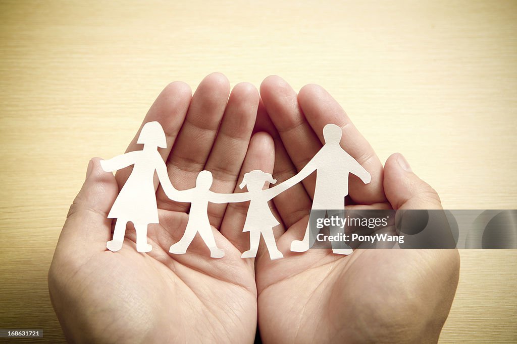 Paper family in hands with wooden texture background