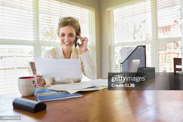 beautiful woman looking at a document while on the phone - 40 year old woman blonde blue eyes stock pictures, royalty-free photos & images