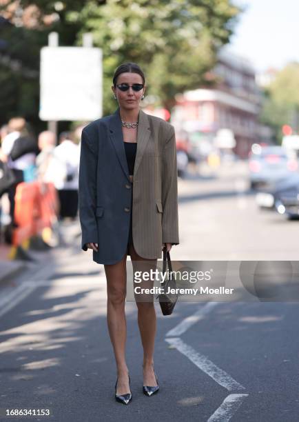 Fashion Show guest was seen wearing black shoes with a silver tip, a brown leather bag, an oversized grey blazer, a short black skirt and a cropped...