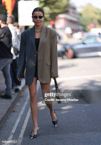 Fashion Show guest was seen wearing black shoes with a silver tip, a brown leather bag, an oversized grey blazer, a short black skirt and a cropped...