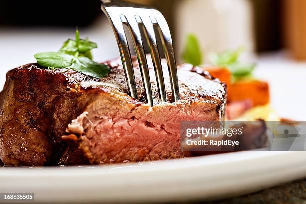 tender and juicy, a fork pierces grilled beef fillet - gefilleerde biefstuk stockfoto's en -beelden