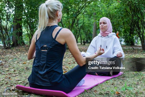 sitting in sukhasana position, two charming female athletes practice yoga in serene park surroundings - moment of silence stock pictures, royalty-free photos & images