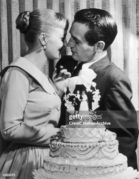 American actors and newlyweds Paul Newman and Joanne Woodward kiss behind a wedding cake during their wedding reception at the El Rancho...