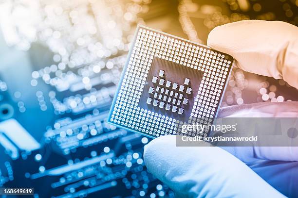 technician holding chip over defocused circuit board - mother board stock pictures, royalty-free photos & images