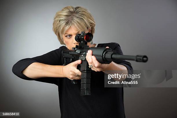 ältere frau aming einem gewehr auf grauem hintergrund. - sportschießen stock-fotos und bilder