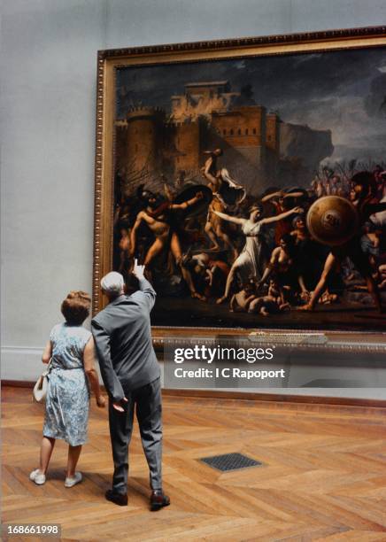 Two museum-goers study the painting, 'The Intervention of the Sabine Women' by Jacques-Louis David at The Louvre in 1964 in Paris, France.