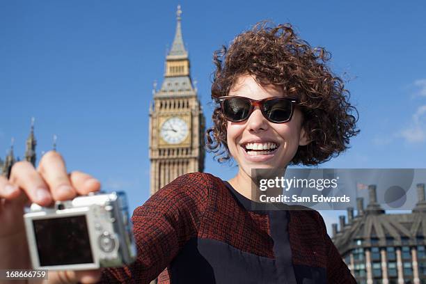 smiling woman taking self-portrait with digital camera below big ben clocktower - monuments in london stock pictures, royalty-free photos & images