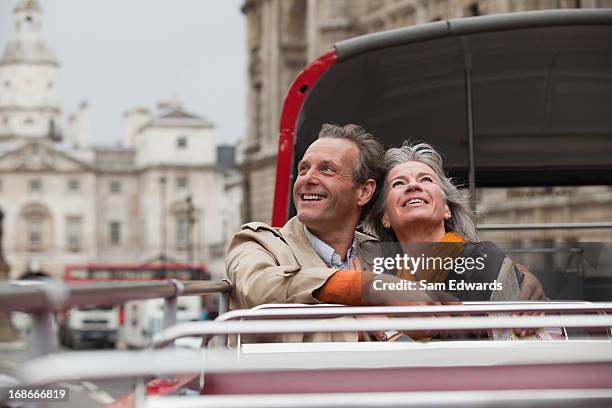 smiling couple looking up on double decker bus in london - london bus stock pictures, royalty-free photos & images