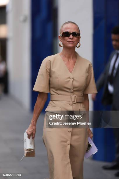 Fashion Show Guest was seen wearing brown shades, a beige and white Hermes bag, a beige coat, yellow gold earrings as well as a pudple notebook...