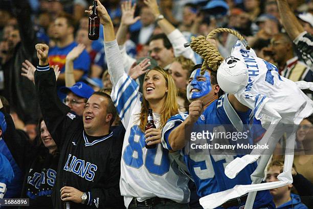 Female Detroit Lion fan celebrates with a Bud Light beer bottle in each hand as a male fan uses a rope noose to hang a blow up skeleton wearing a...