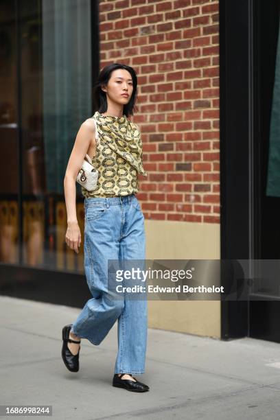 Guest wears a beige large scarf worn as a tank top with printed geometric patterns, blue jeans, black flat ballet shoes, outside Tibi , during New...