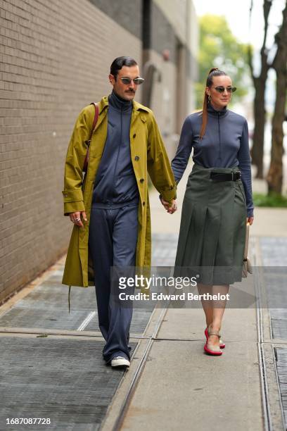 Guest wears a khaki trench coat, a navy blue sportswear outfit ; a guest wears a navy blue sportswear sweated, a green pleated midi skirt, red shoes,...