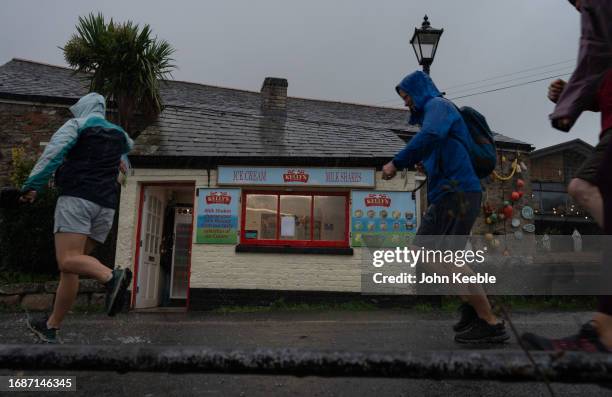 People run past an ice cream shop during a heavy rain downpour in Charlestown on September 17, 2023 in St Austell, Cornwall, United Kingdom.