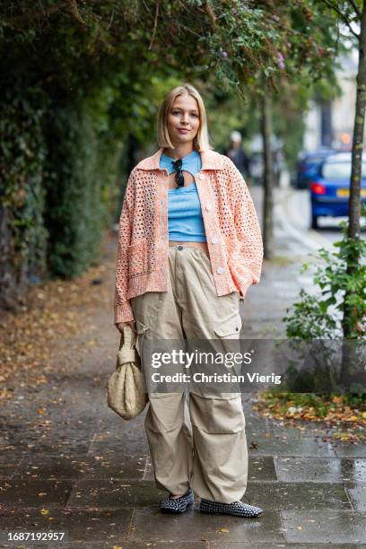 Hollie Mercedes Peters is seen wearing salmon colored cardigan, beige pants with side pockets, Bottega Veneta bag, blue cut out top outside...