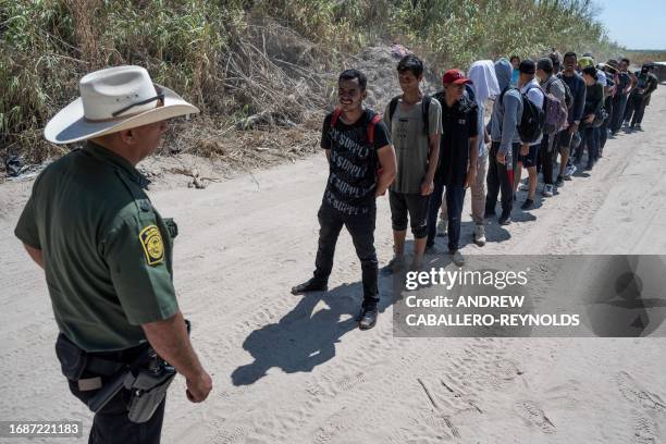 Migrants from Venezuela stand in a line in front of a US Border Patrol agent before walking to a processing area after they crossed the Rio Grande in...