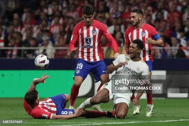 Real Madrid's English midfielder Jude Bellingham reacts to being tackled by Atletico Madrid's Spanish midfielder Saul Niguez during the Spanish Liga...