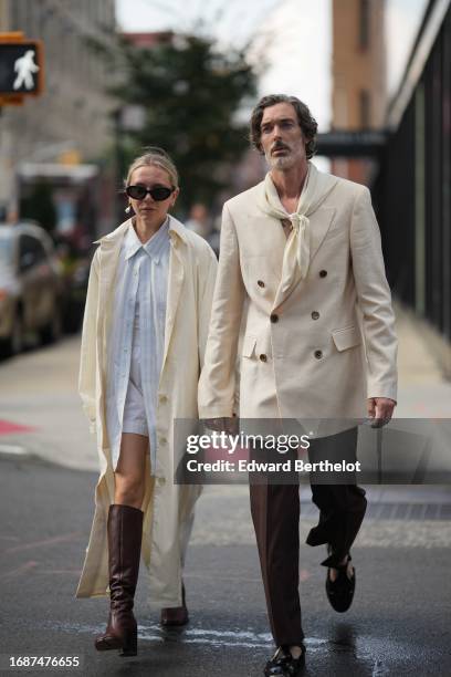 Guest wears sunglasses, a pale blue striped shirt, mini shorts, a white trench coat, brown knee-high leather boots ; a guest wears a scarf, a double...