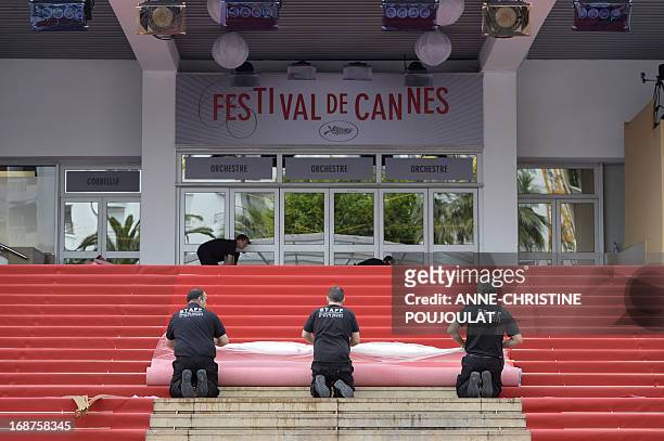 Workers unroll the red carpet at the entrance of the Palais des Festivals on the opening day of the 66th edition of the Cannes Film Festival on May...