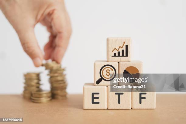 wooden cube with ETF text , Exchange Traded Fund and blurred hand with stack of coins. for business finance conceptual
