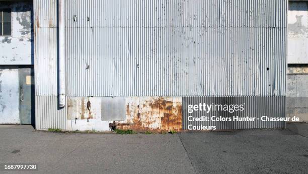 weathered wall in corrugated metal sheets, painted and patinated in gray, with door and asphalt street in montreal, quebec, canada - galvanized stock pictures, royalty-free photos & images