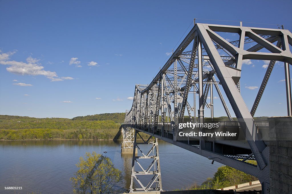 Steel bridge over calm waters near green trees.
