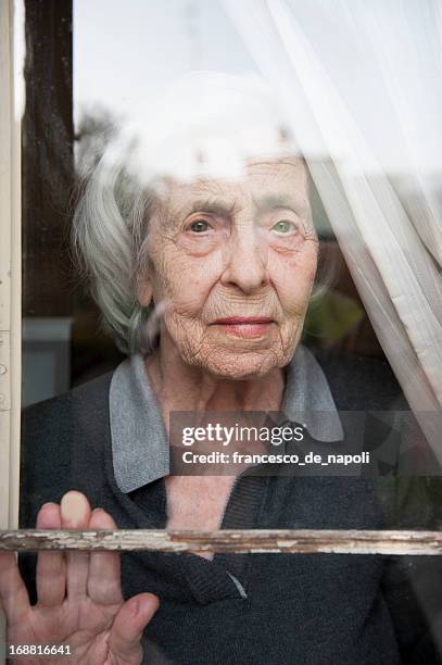 senior woman looking through a window looking lonely - old woman by window stock pictures, royalty-free photos & images