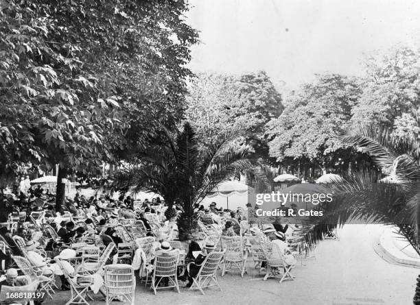 People sitting outdoors in white cane chairs in Vichy, France, 1930s.