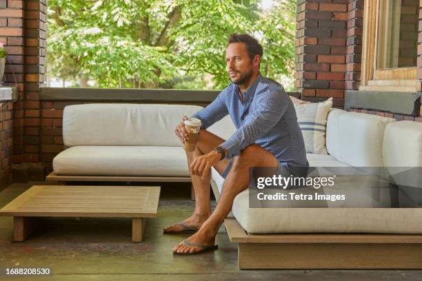 mid adult man relaxing on sofa on patio - calções azuis - fotografias e filmes do acervo