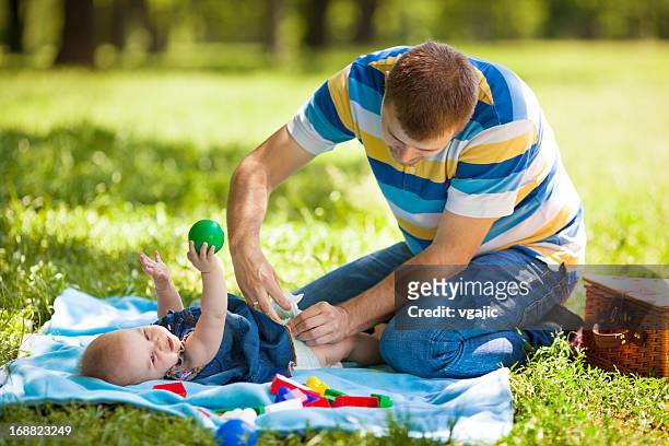 father changing baby diaper outdoors. - changing nappy stock pictures, royalty-free photos & images