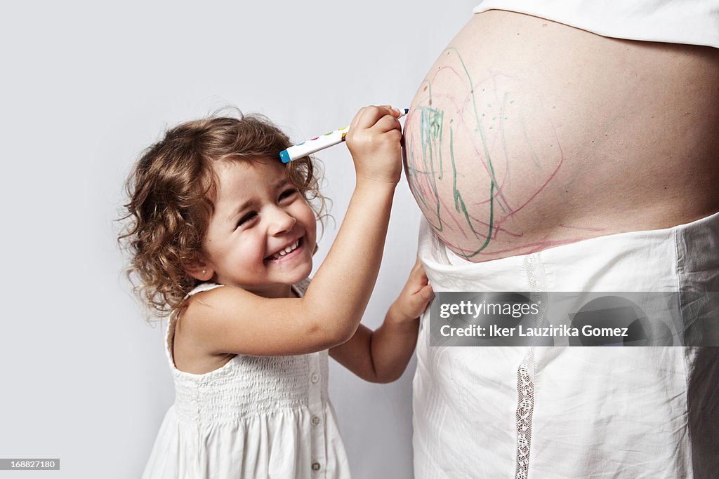 Girl painting her mother´s pregnant belly