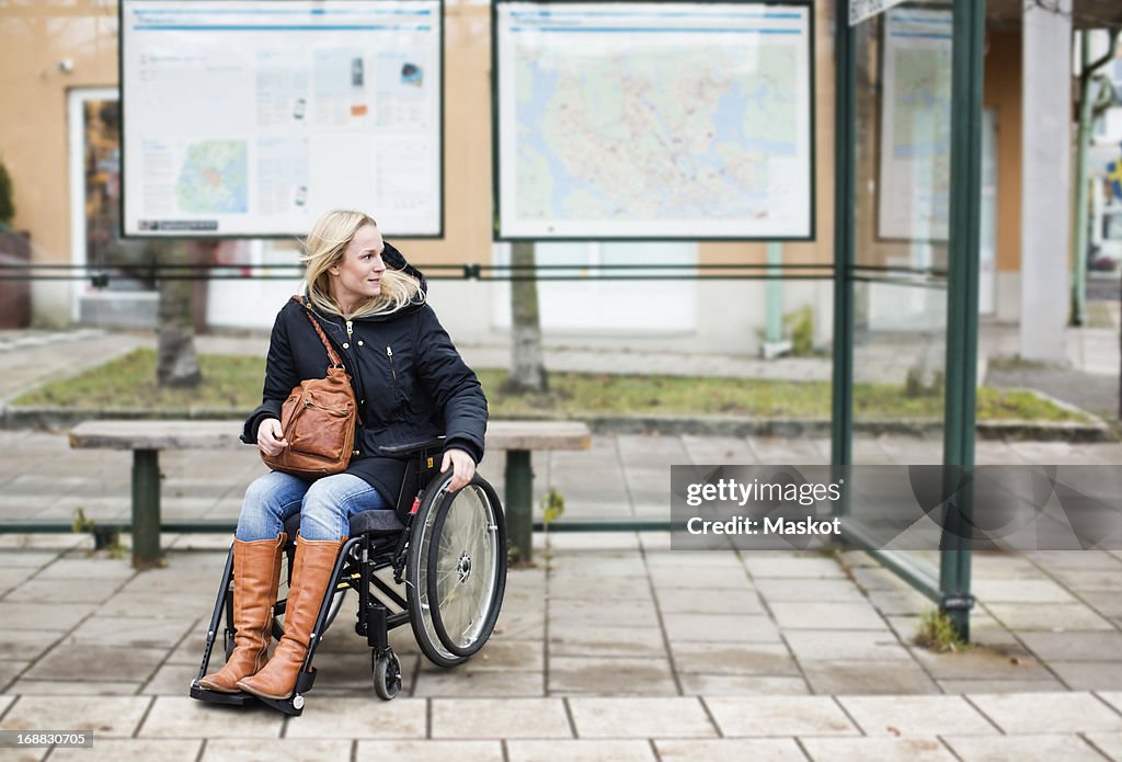 Disabled woman in wheelchair waiting at bus stop