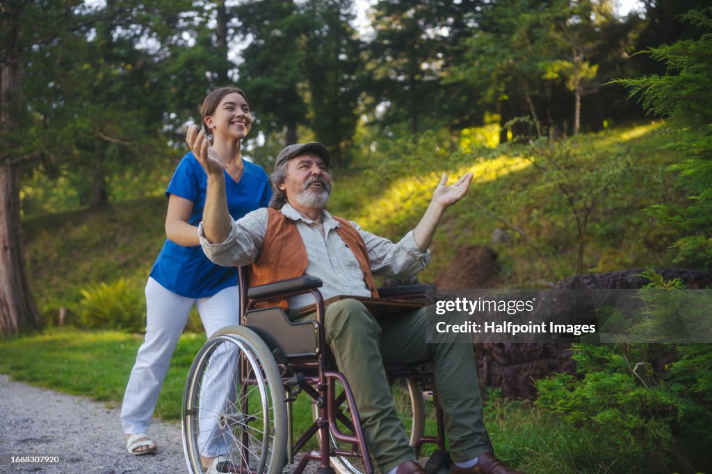 Young caregiver pushing patient on wheelchair from a nursing home in the park.