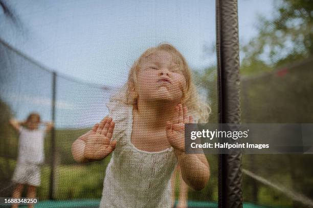 little girl standing on a trampoline, pressing her face against the safety net. - sicherheitsnetz stock-fotos und bilder