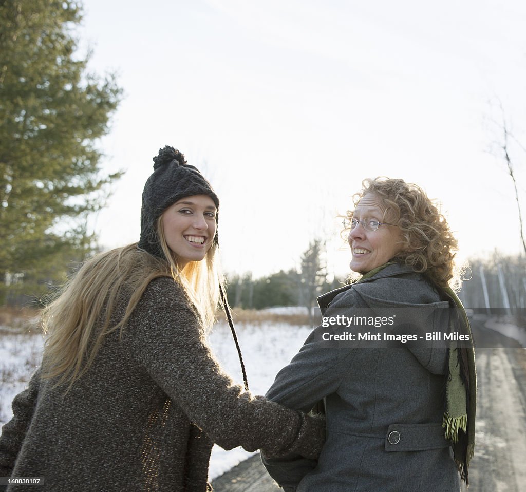 A mother and daughter arm in arm walking along a path and looking over their shoulders.