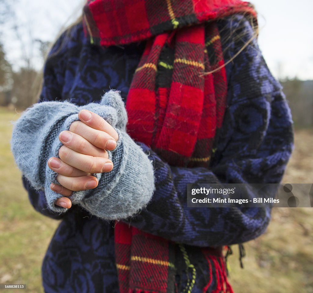 A woman in a tartan scarf and knitted woollen mitts, keeping her hands warm in cold weather.