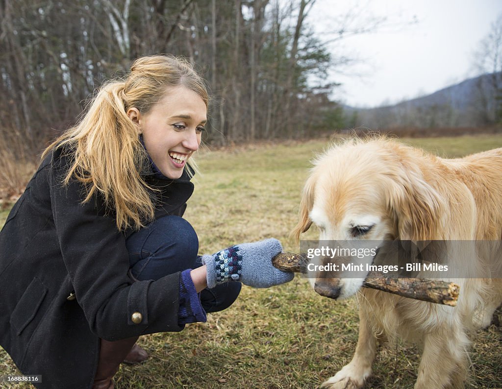 A young woman outdoors in the winter, on a walk with a golden retriever dog. 