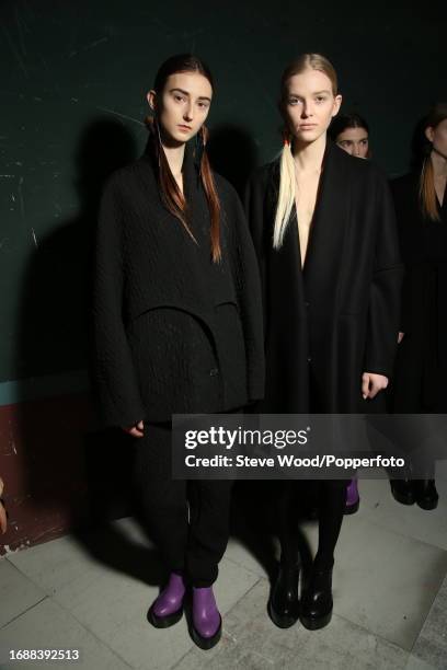 Backstage at the Chalayan show during Paris Fashion Week Autumn/Winter 2016/17, two models wear minimalist black wool coats, one in a textured wool...