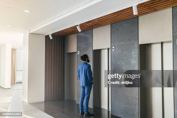 businessman is standing in corridor hall in office building and waiting for elevator - lift stock pictures, royalty-free photos & images