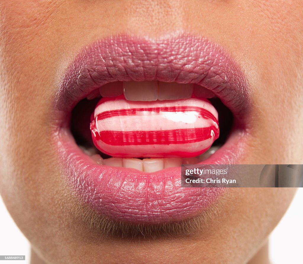 Close up of woman with pink lipstick biting hard candy