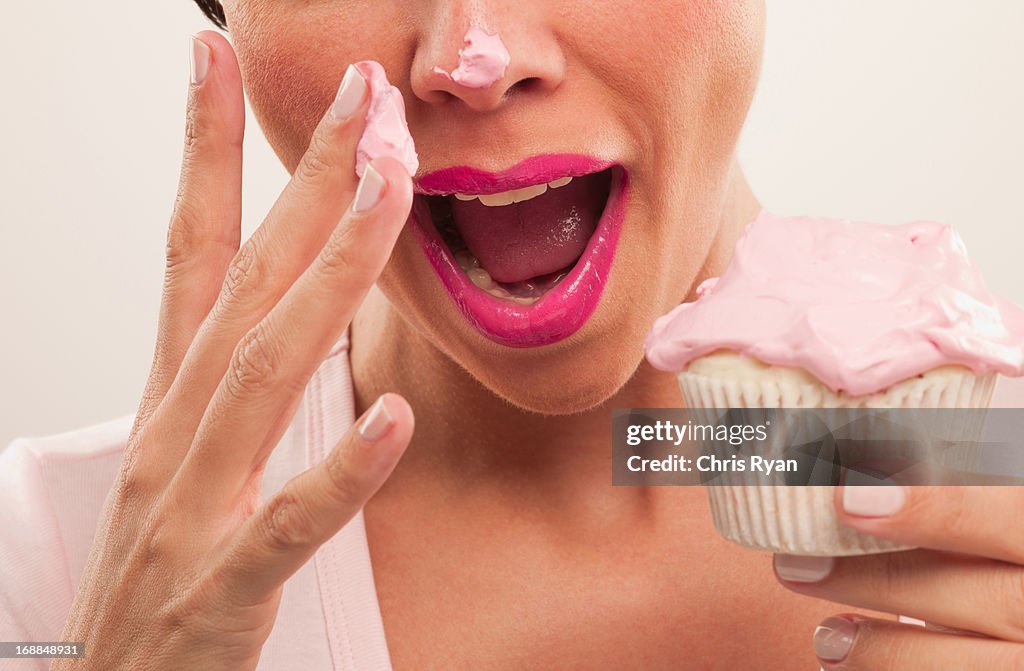 Woman with pink lipstick and frosting on nose eating cupcake