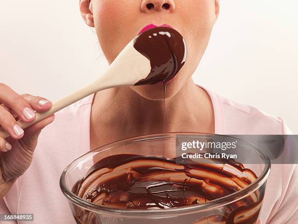 woman with pink lipstick licking chocolate batter from wooden spoon - chris chocola stockfoto's en -beelden