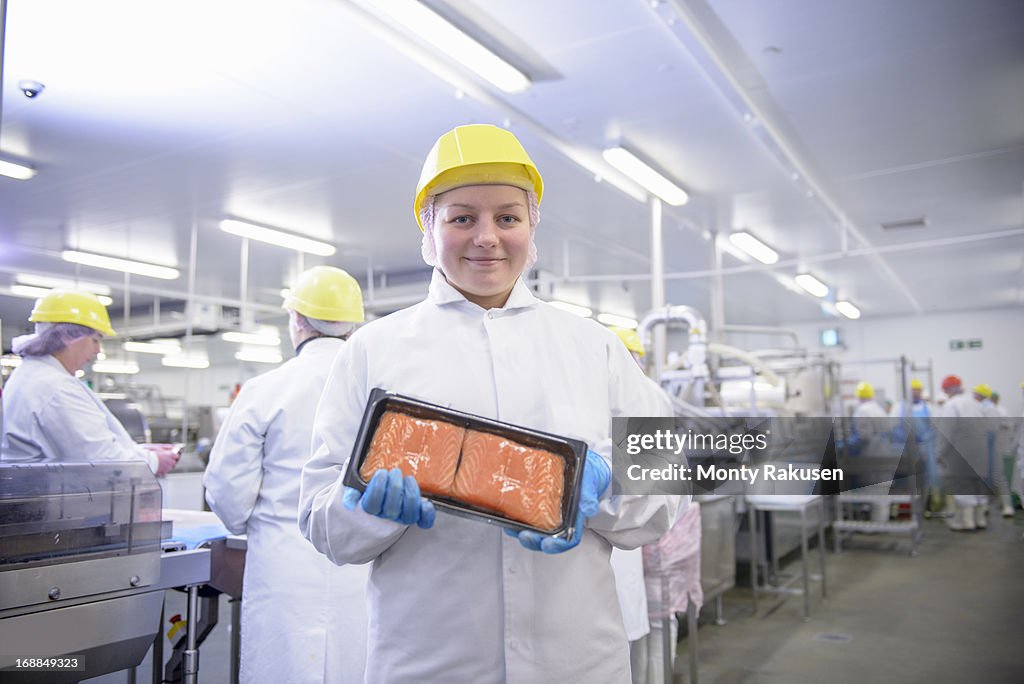 Portrait of worker holding pack of salmon fillets in food factory