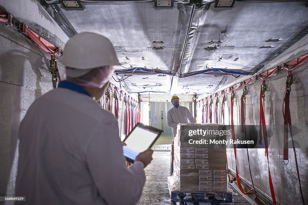 Worker checking products into freezer truck of food factory with tablet