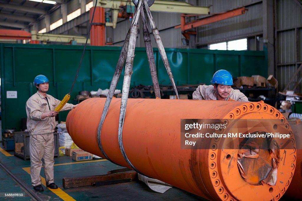 Workers moving large cylinder in hydraulics factory