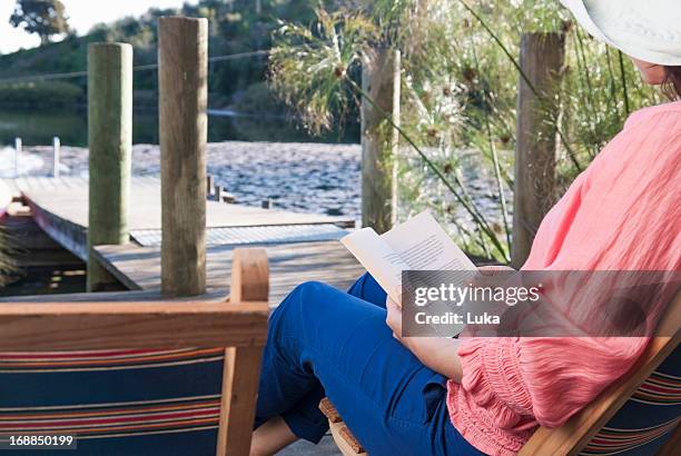 woman reading in lawn chair on deck - beach deck chairs stock-fotos und bilder