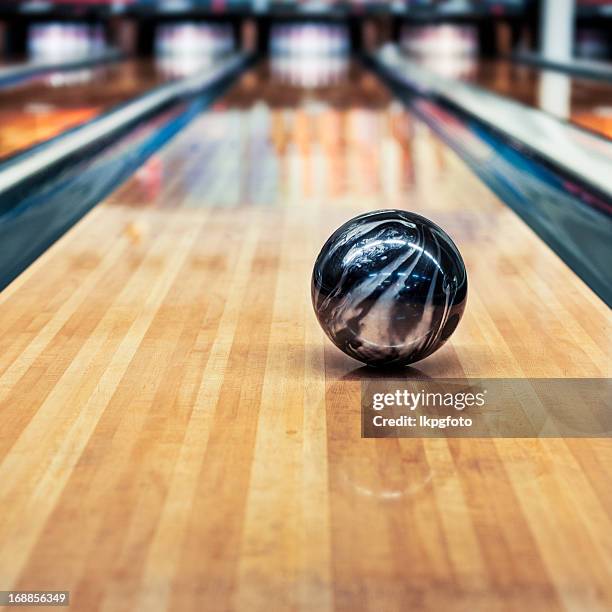 a black and silver bowling ball rolling down the lane - bowlingbal stockfoto's en -beelden