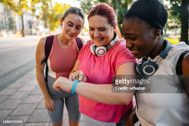 three young female friends checking fitness activity on the smartwatch after exercising in the park - 3 hours stock pictures, royalty-free photos & images