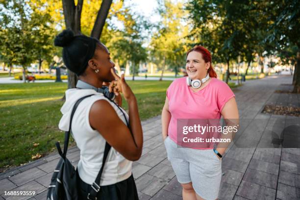 two young female friends talking before jogging in the park - slightly overweight stock pictures, royalty-free photos & images