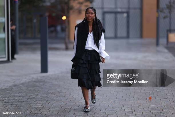 Kenya Hunt is seen wearing long transparent earrings, a black wool pullover around the neck, a white skirt, a black stepped knee-length skirt with...