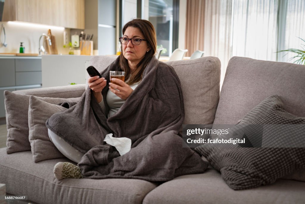 Sick woman resting on sofa and drinking hot tea